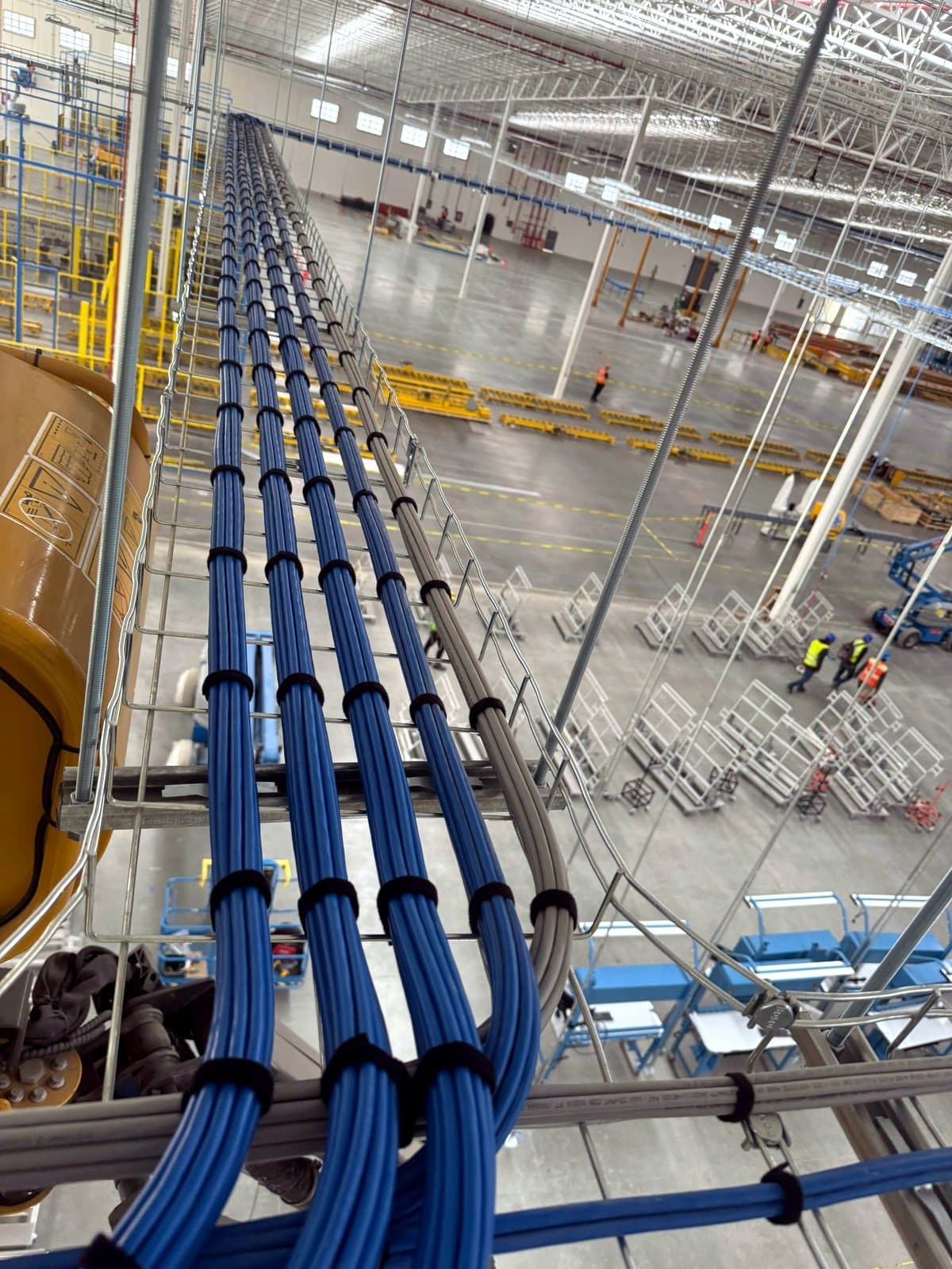 Fotografía de instalación ERCONNECT de una bajada de canalización con cableado estructurado en una nave industrial de gran altura durante la obra