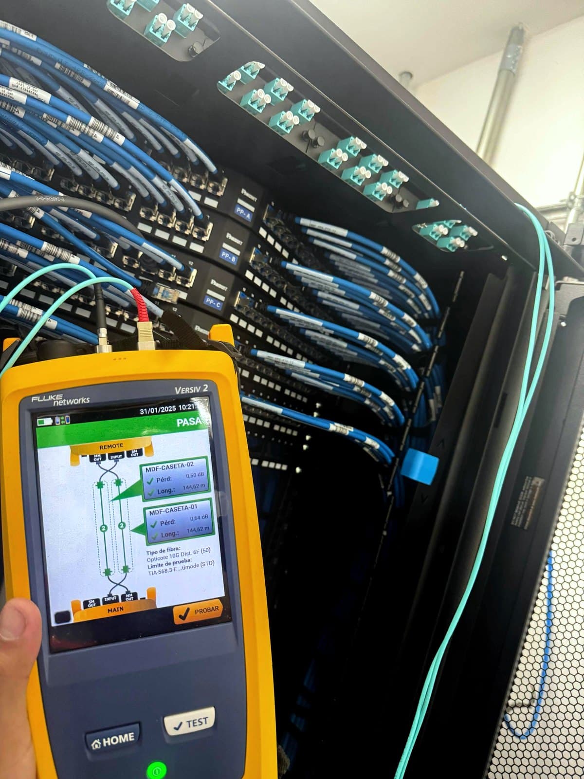 Fotografía de instalación ERCONNECT: certificación de enlaces de fibra óptica con la plataforma Fluke Networks Versiv mostrando resultado PASA para enlaces de 144.62 m con pérdidas de 0.50 y 0.64 dB contra el límite de prueba seleccionado para el proyecto
