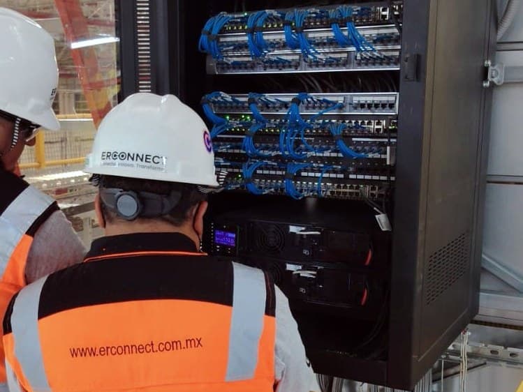 Fotografía del proyecto con dos técnicos de ERCONNECT frente a un IDF abierto, revisando los UPS de rack del gabinete