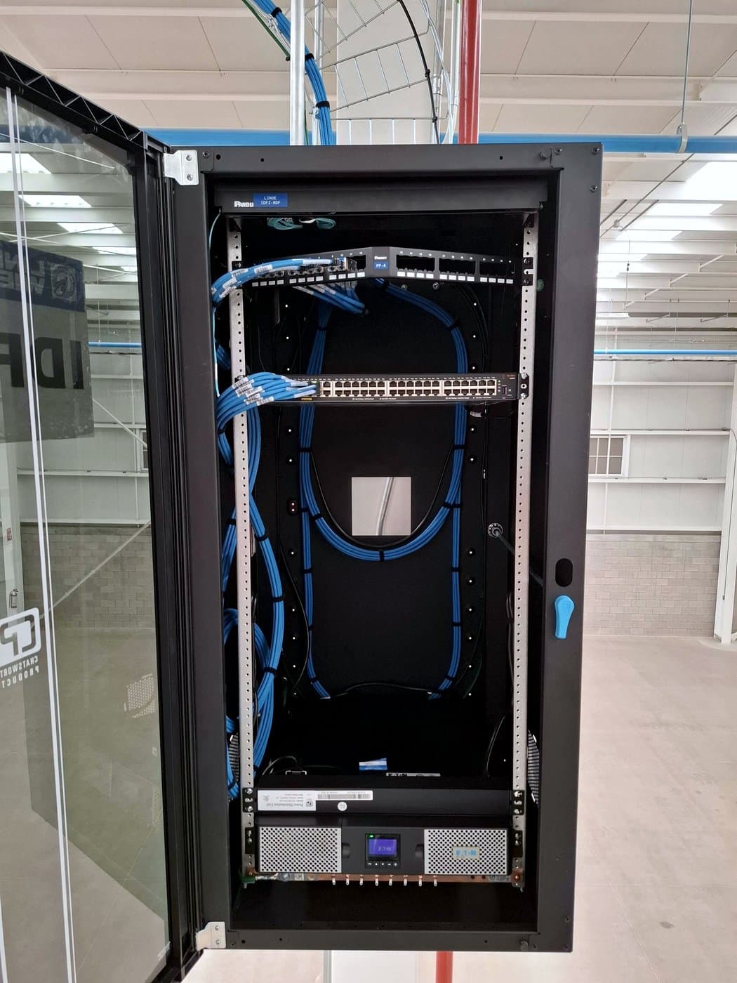 Fotografía de instalación ERCONNECT: gabinete de telecomunicaciones en cuarto técnico con vista a nave industrial