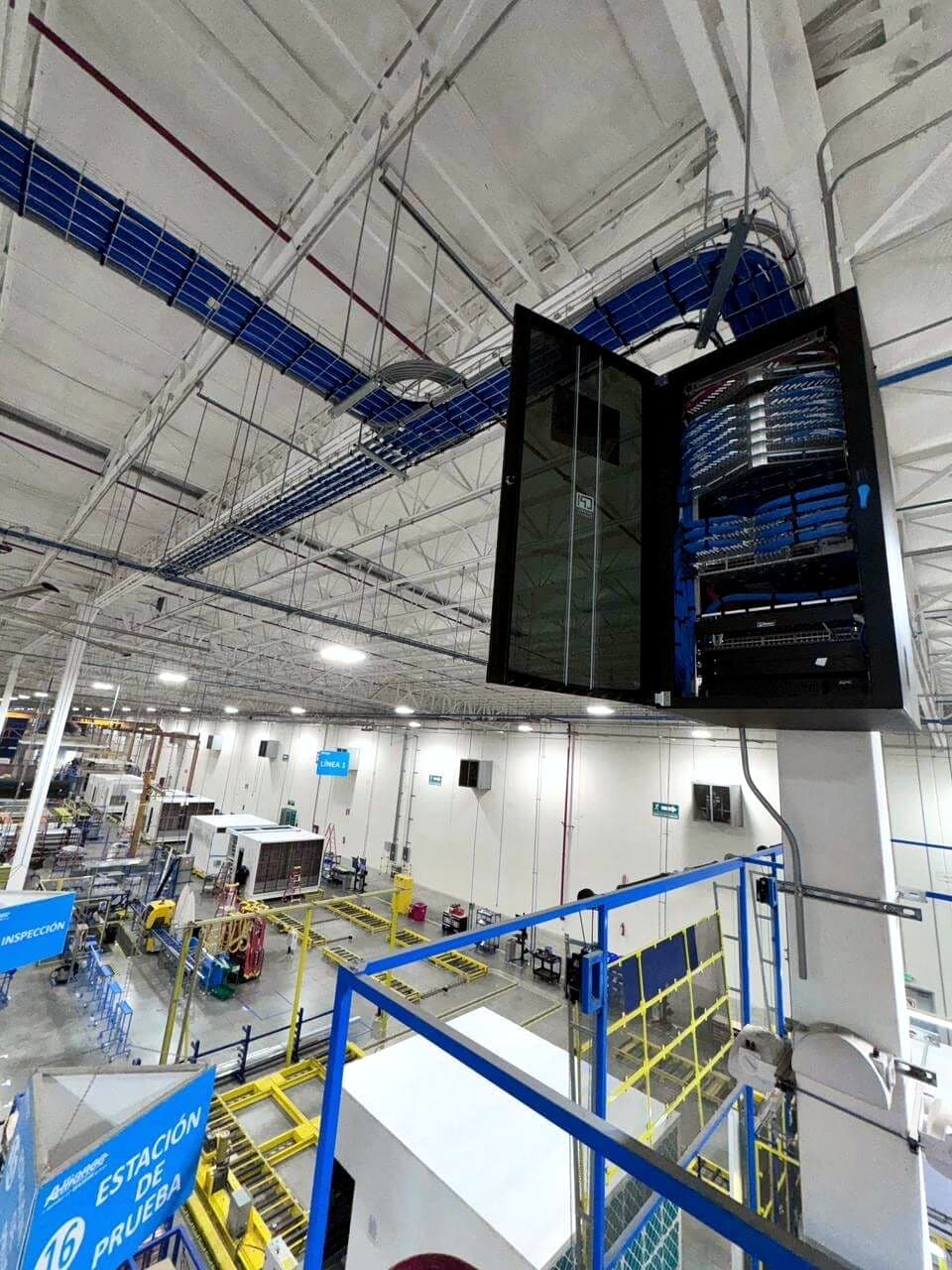 Fotografía de instalación ERCONNECT de un gabinete de telecomunicaciones satélite montado en altura sobre el piso de producción de la planta, con charola de cableado al techo