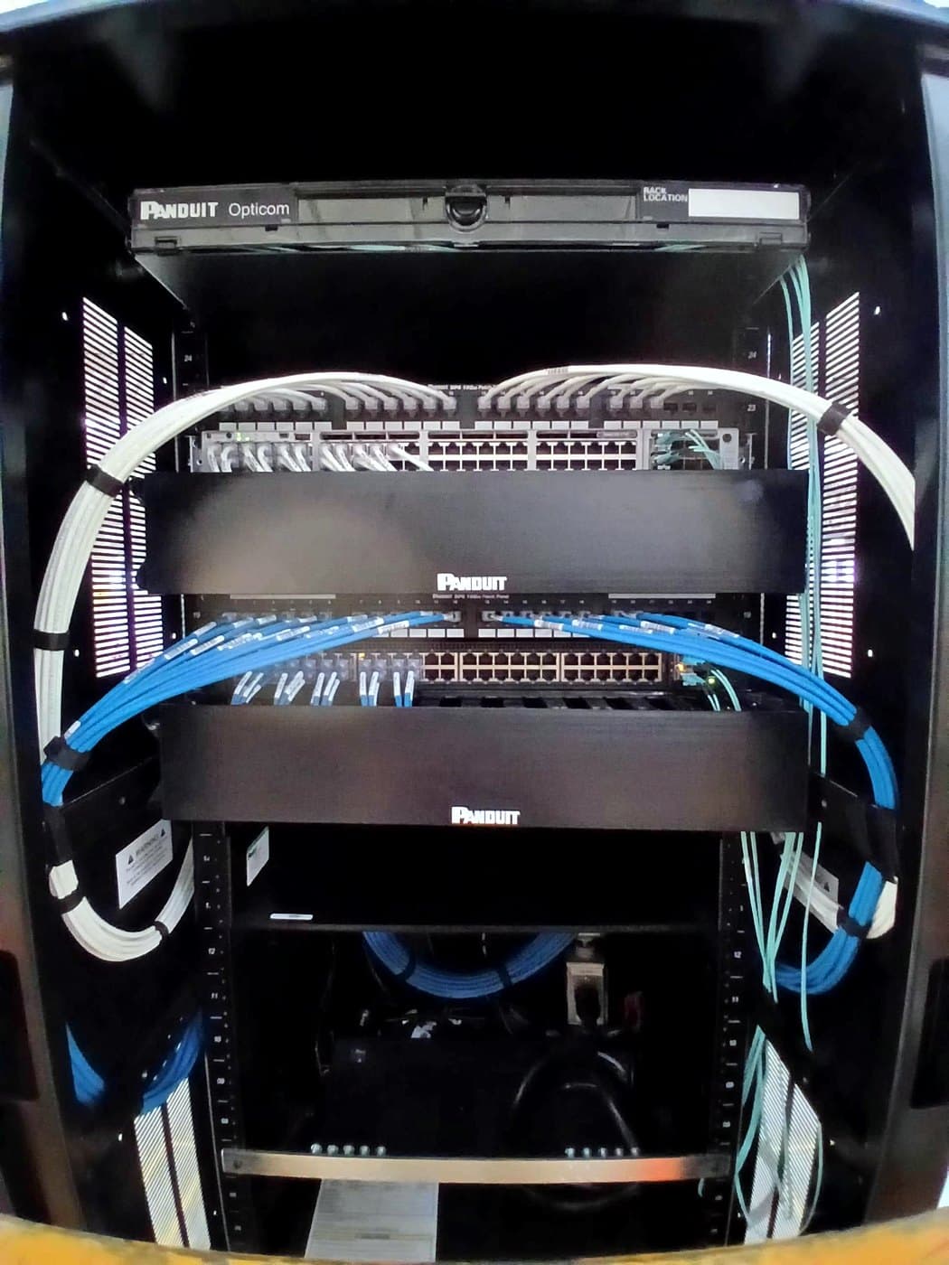 Fotografía de instalación ERCONNECT: gabinete satélite con paneles Panduit, cordones blancos y azules administrados y piso de planta al fondo