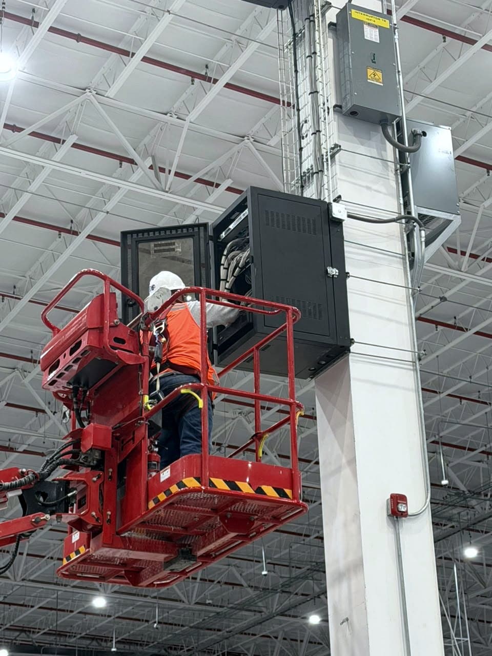 Fotografía de obra con un técnico en plataforma de elevación trabajando en un IDF montado en lo alto de una columna de un centro de distribución