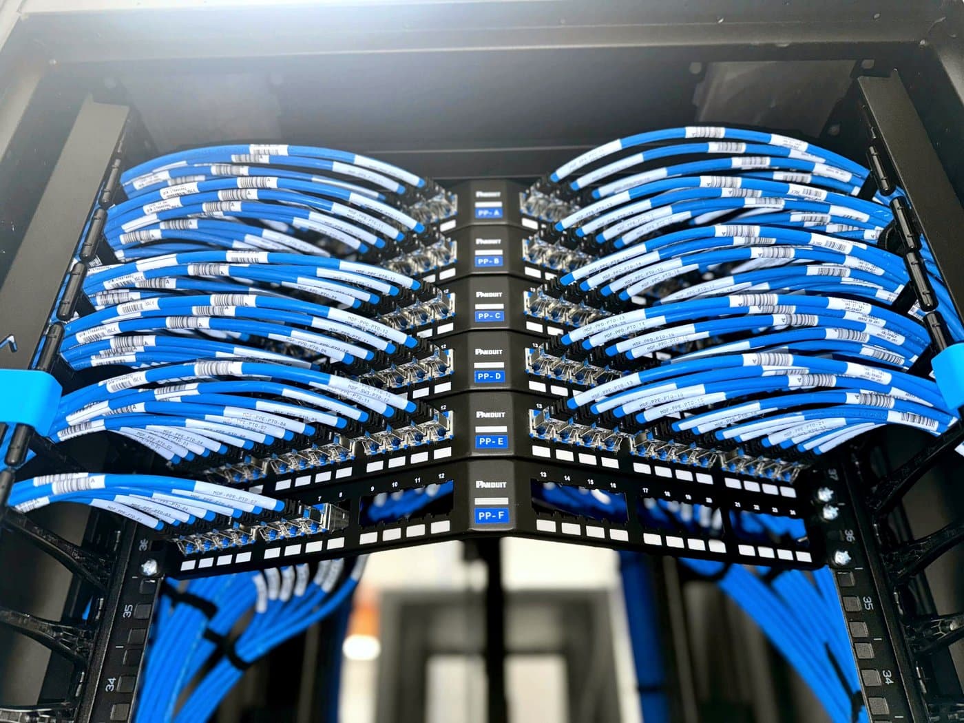 Fotografía de instalación ERCONNECT: paneles de parcheo terminados con cordones azules peinados y etiquetados, listos para certificación punto por punto