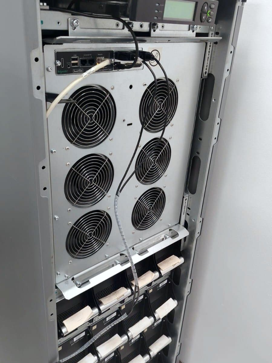 Fotografía de obra con un UPS trifásico Schneider Galaxy VS abierto durante su mantenimiento preventivo, con sus ventiladores y módulos de batería a la vista